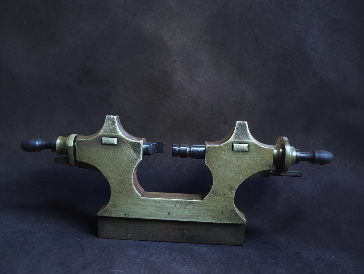 Antique Jacot tool brass frame standing upright with two opposing steel runners and dark wooden handles
