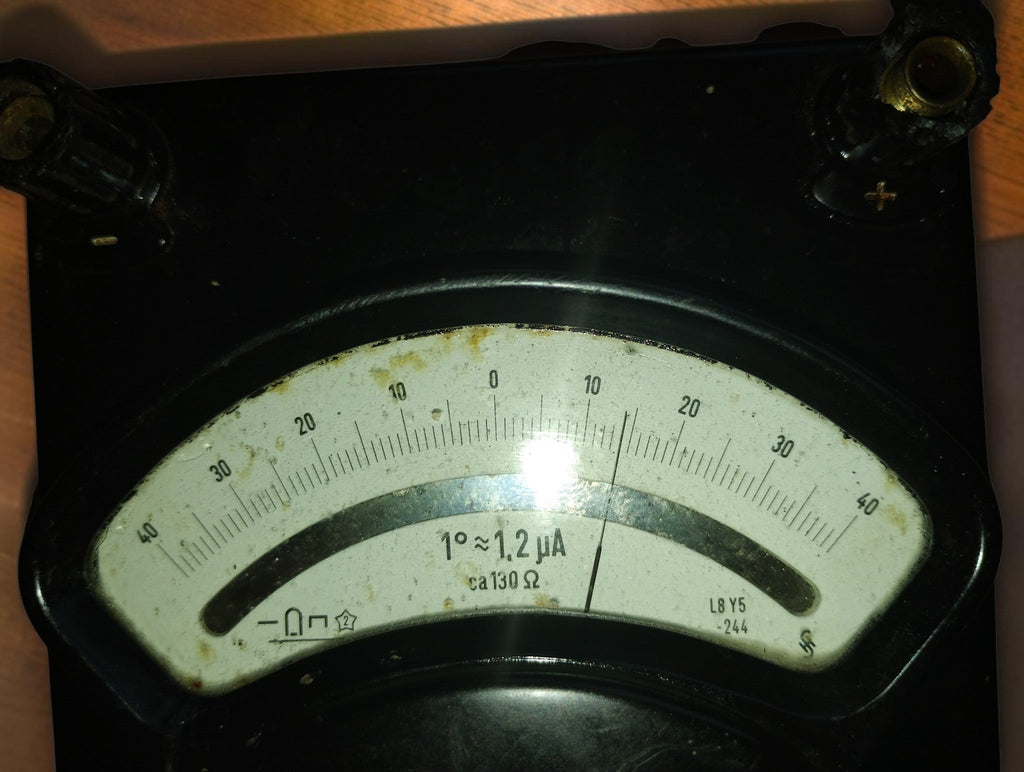 Galvanometer dial close-up showing the center-zero scale, 1° ≈ 1.2 μA marking, and age-related discoloration.
