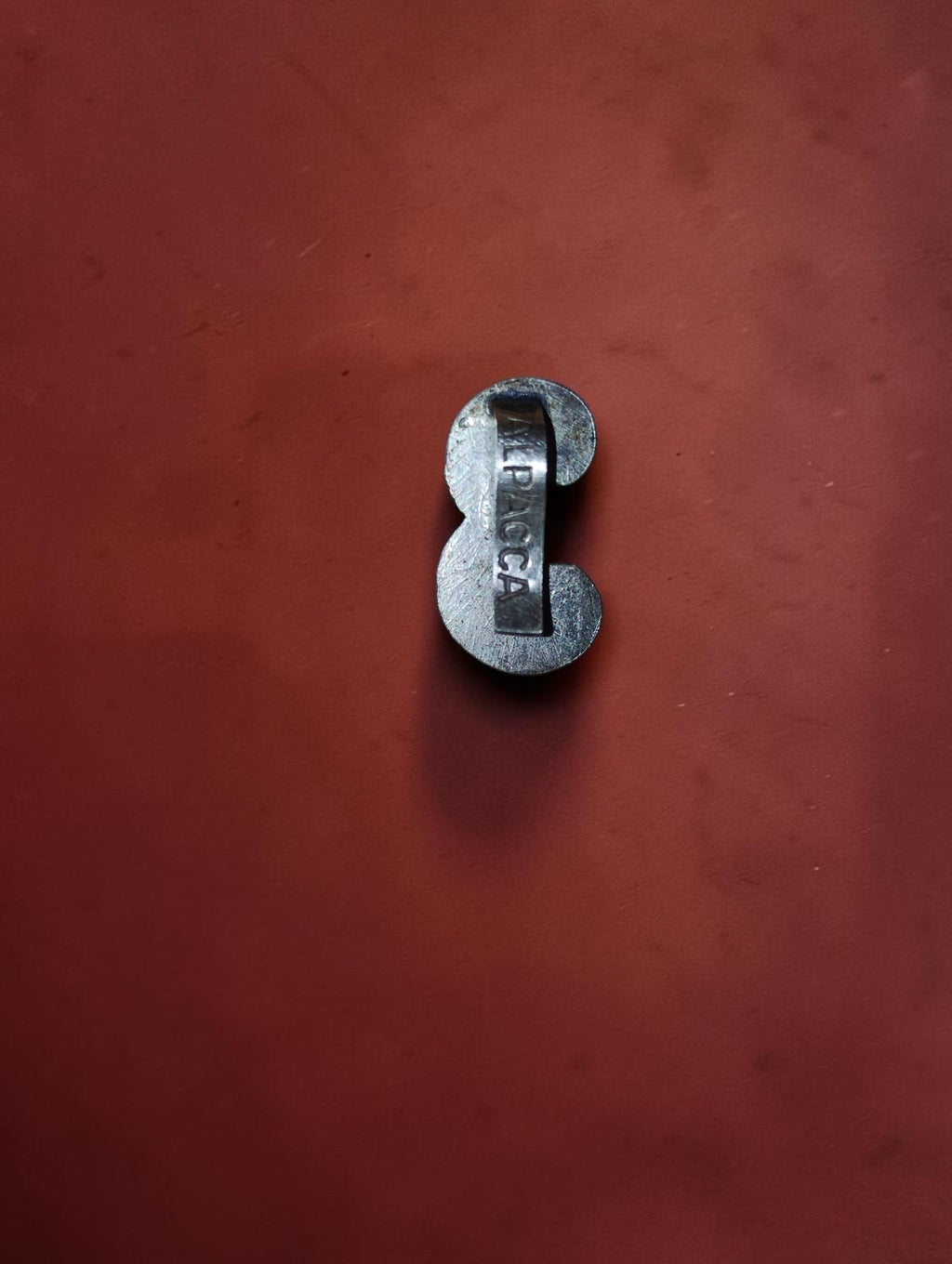 Back of a vintage metal clock dial numeral showing the ALPACCA inscription and attachment clip.
