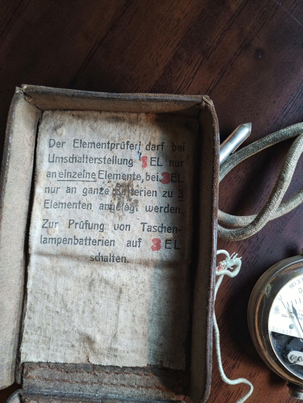 German instruction label inside the battery tester case, describing settings for one cell and three-cell batteries.
