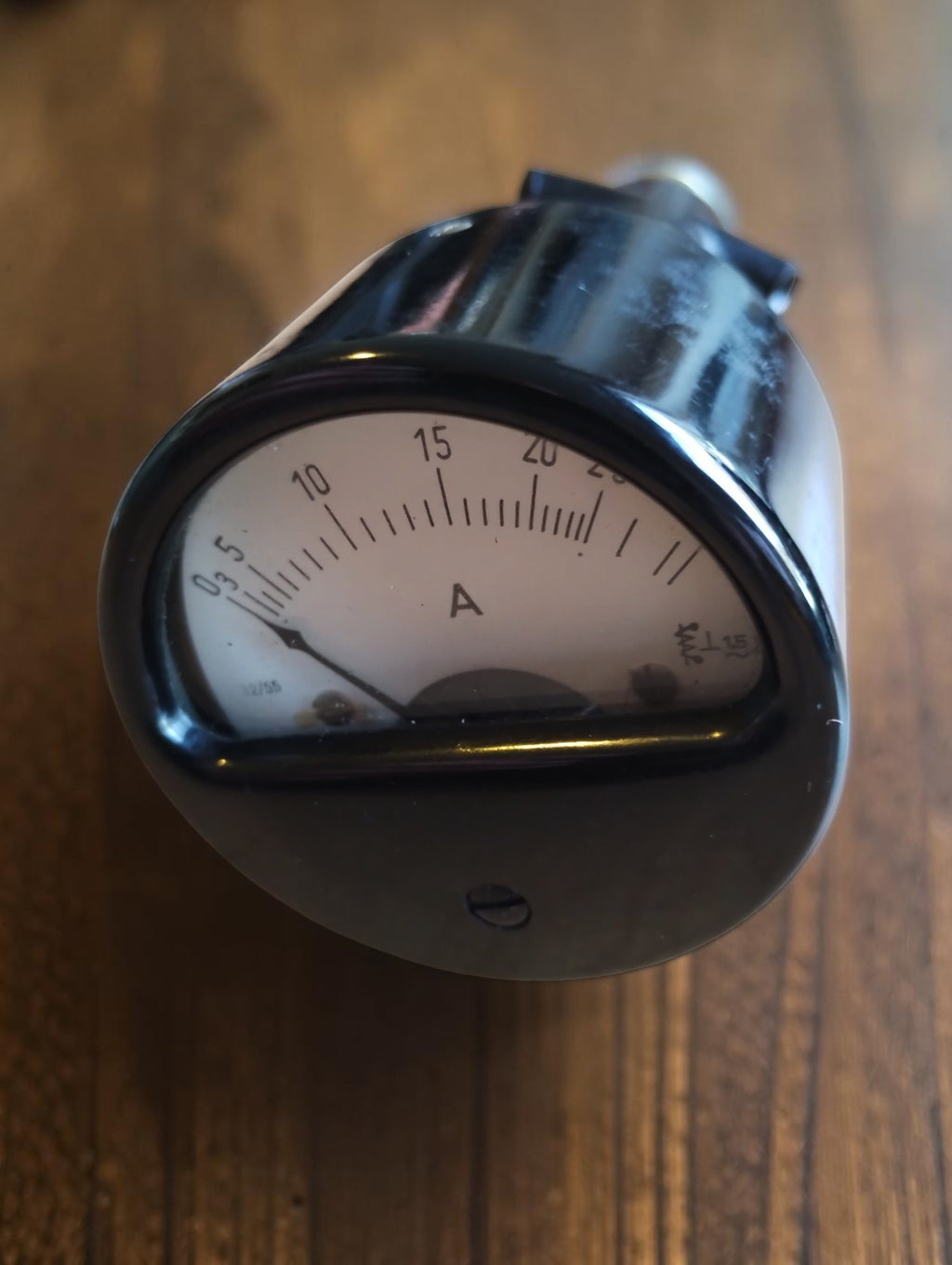 Front view of a vintage test ammeter with a curved analog dial and black cylindrical housing.
