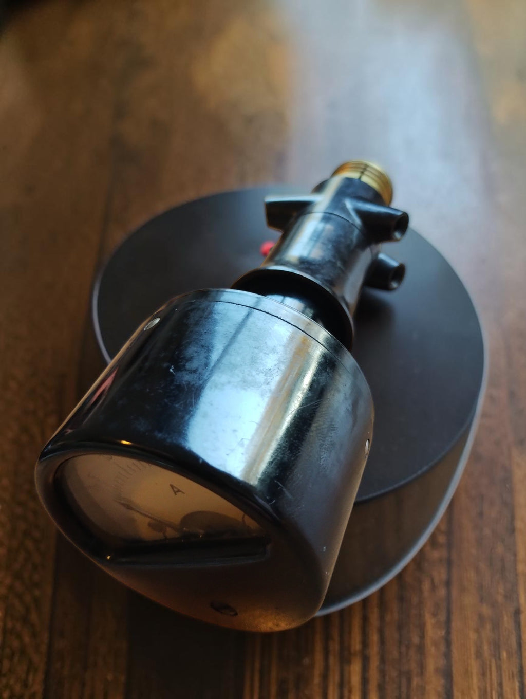 Side view of a vintage test ammeter with a black housing, analog dial and Edison screw base.
