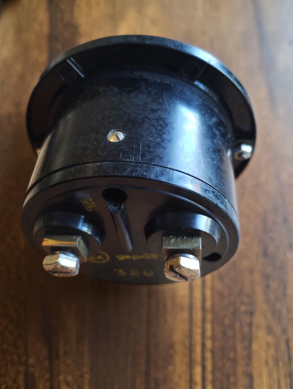 Rear view of a vintage round panel meter showing its black cylindrical housing and two threaded terminals.
