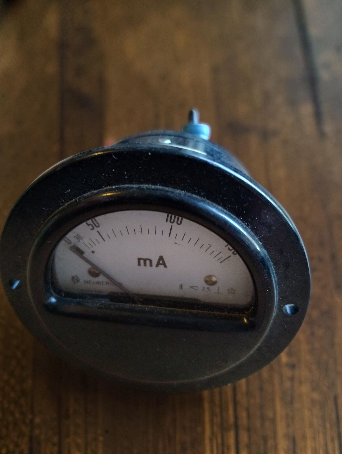 Angled front view of a vintage round milliamp meter with a cream dial and black mounting flange.
