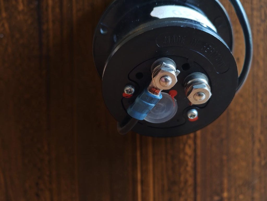 Rear view of a vintage panel meter with two threaded terminals and a wire attached by a blue connector.
