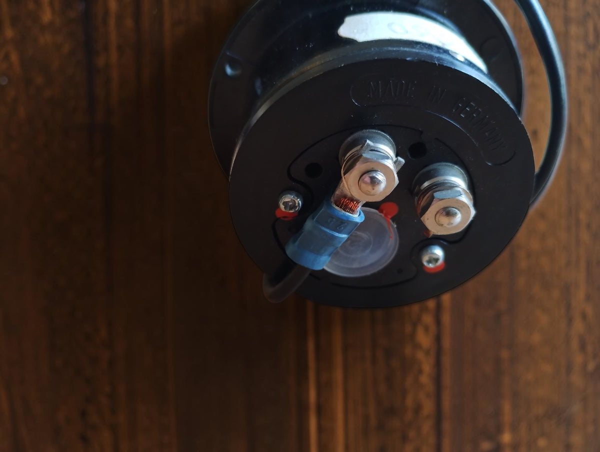 Rear view of a vintage panel meter with two threaded terminals and a wire attached by a blue connector.
