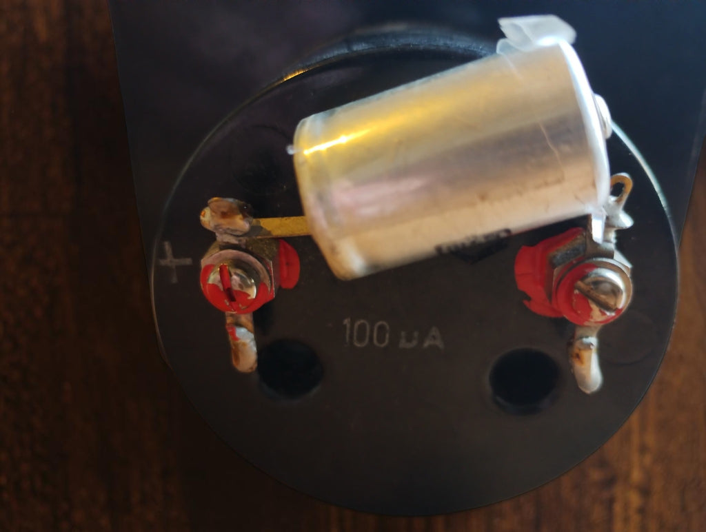 Rear view of a vintage meter marked 100 µA, showing screw terminals and a cylindrical metal component.
