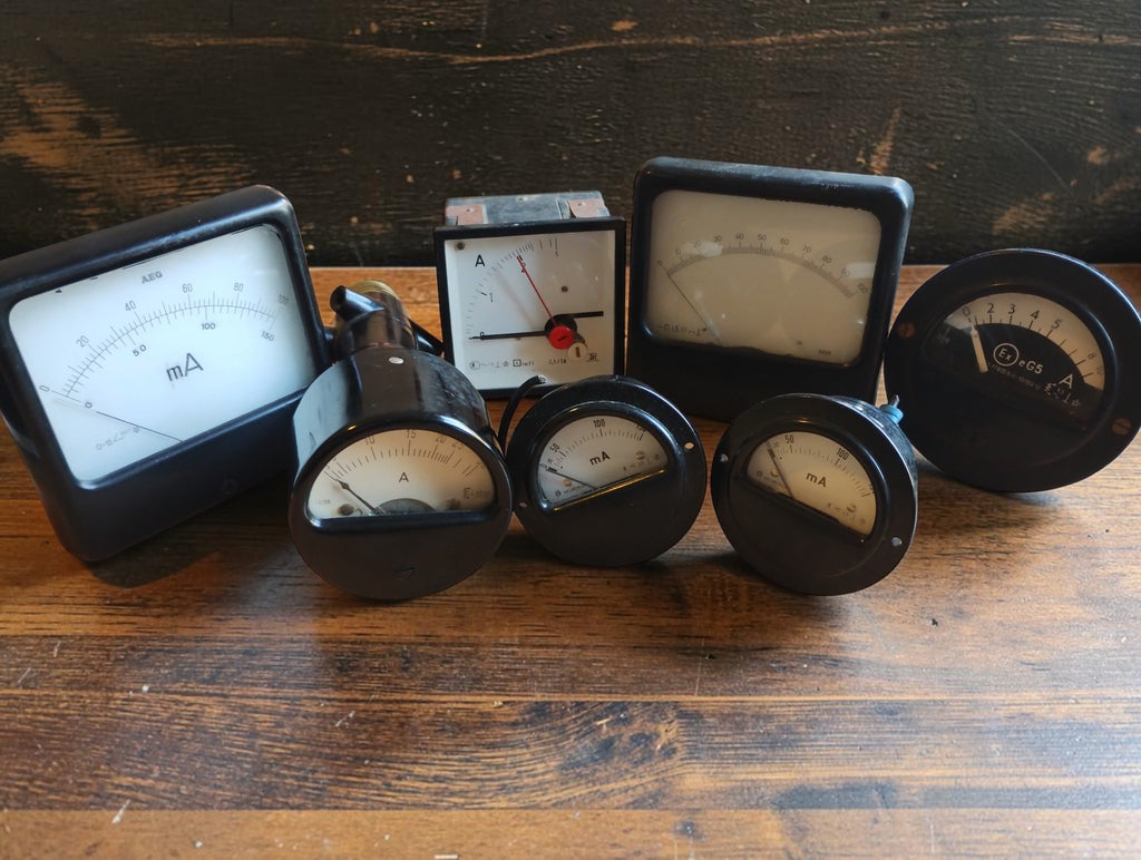 Lot of seven vintage analog panel meters with round and square dials, including AEG milliamp meters.
