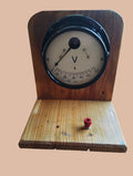Vintage analog AC voltmeter on a wooden stand, showing the full instrument and red terminal on the base.
