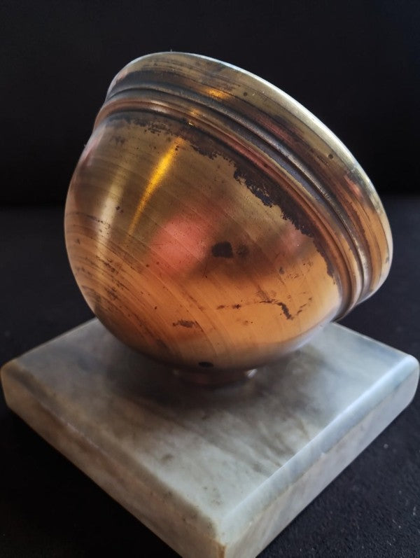 Rounded brass back of the desk barometer showing patina and surface wear, mounted on a marble base.
