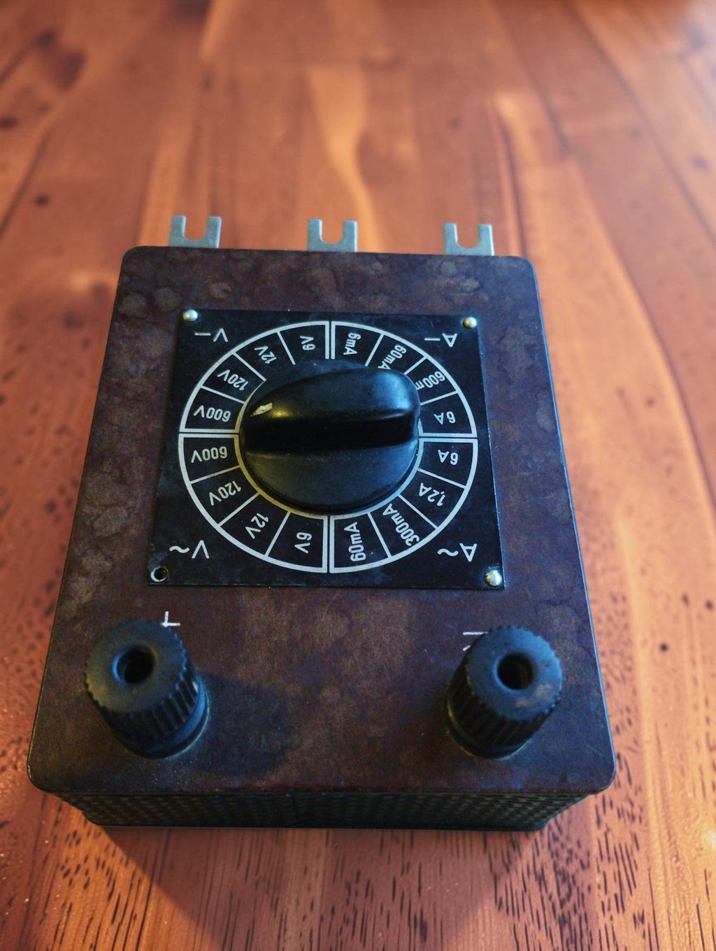 Vintage brown Bakelite range selector with central rotary knob, white electrical markings and two terminal sockets
