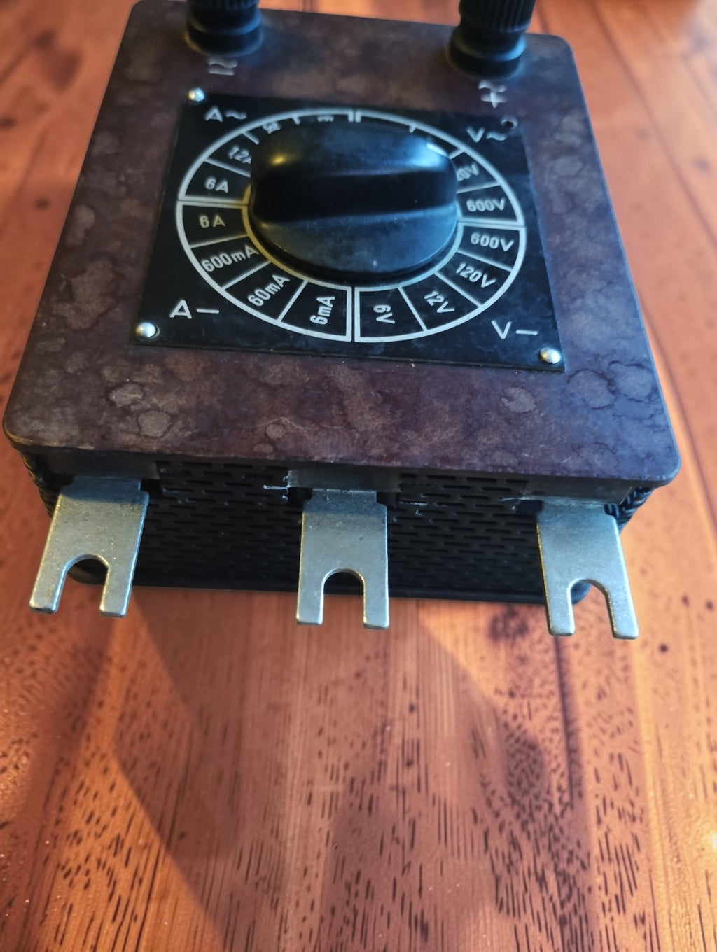 Angled view of vintage Bakelite range selector showing three fork-shaped metal contacts and white voltage and current markings
