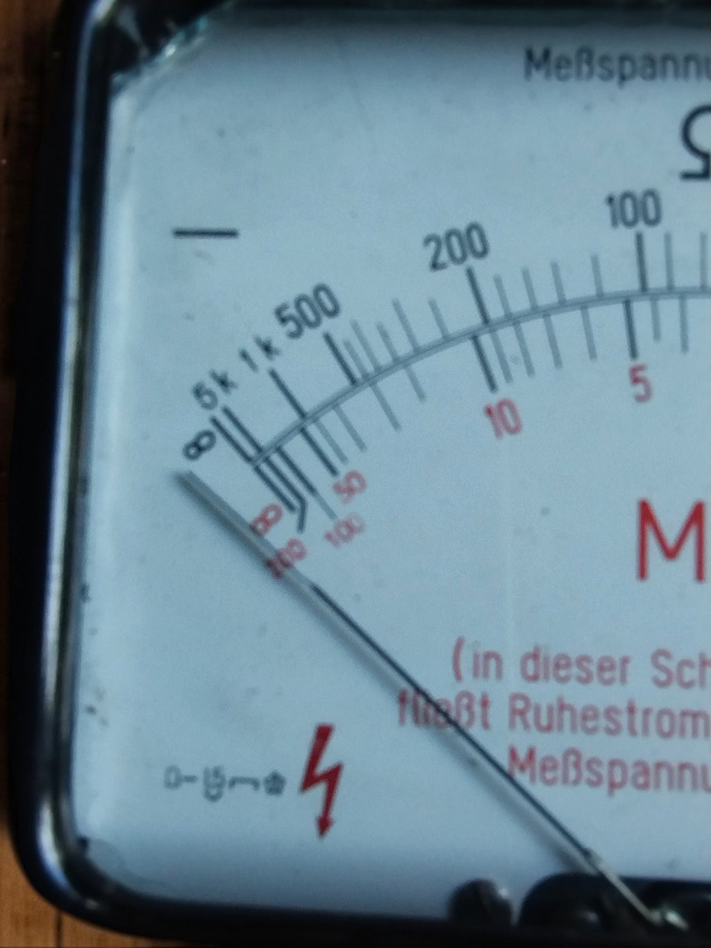 Close-up of the analog resistance scales, pointer, and red electrical warning symbol on the Gossen insulation tester
