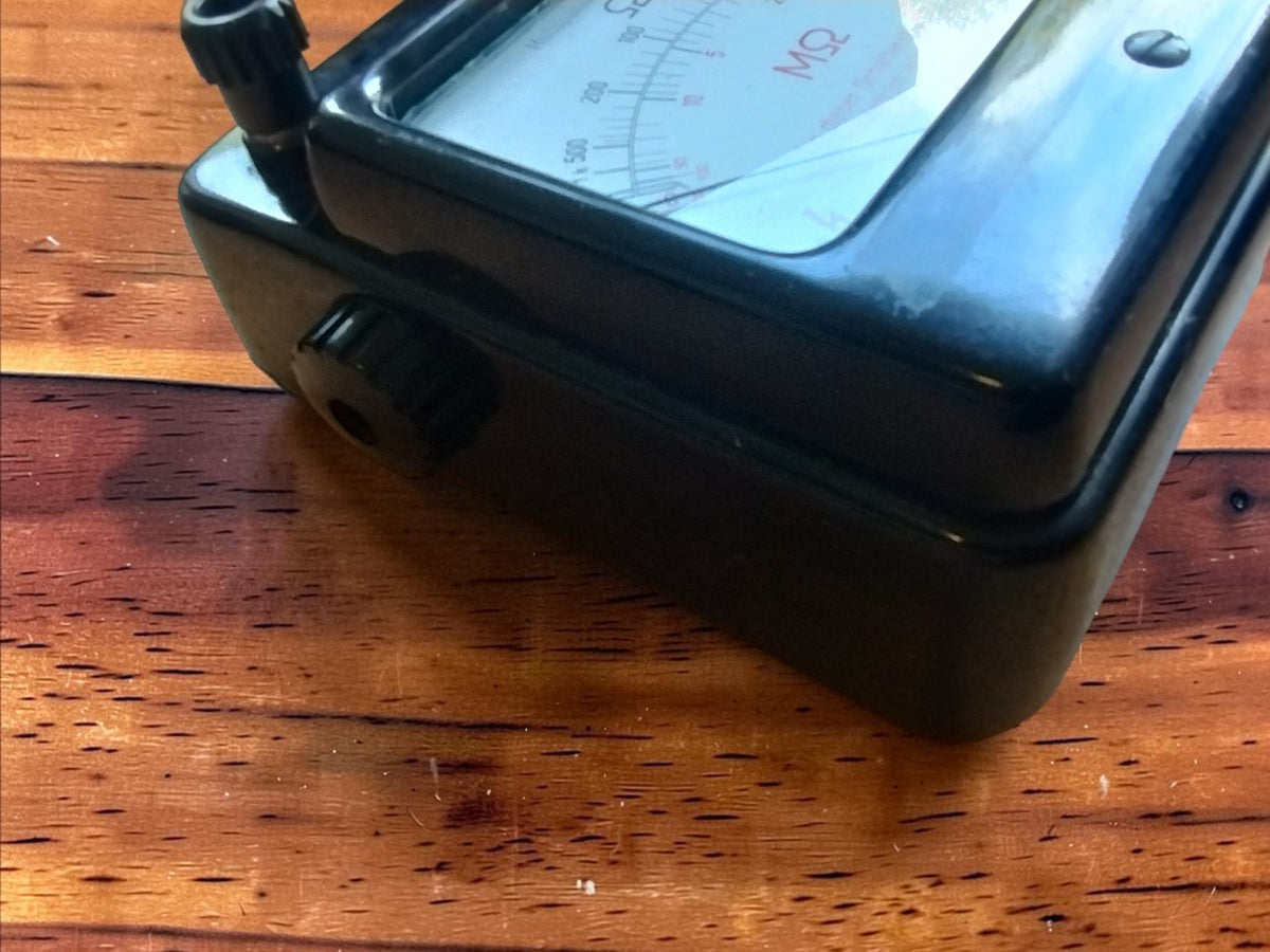 Angled view of the Gossen insulation tester showing the black Bakelite housing, glass dial window, and side control
