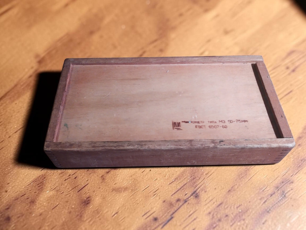 Vintage wooden sliding-lid micrometer case with visible grain, worn edges and stamped Cyrillic markings.
