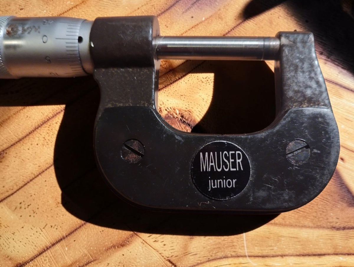Close-up of the MAUSER junior badge on the dark metal micrometer frame
