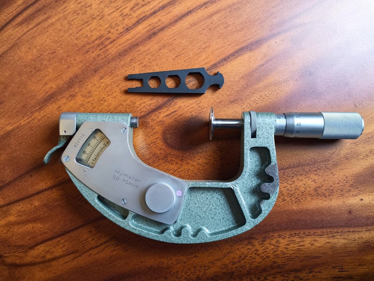 Mymeter 50–75 mm indicating micrometer with its separate adjustment wrench on a wooden surface.
