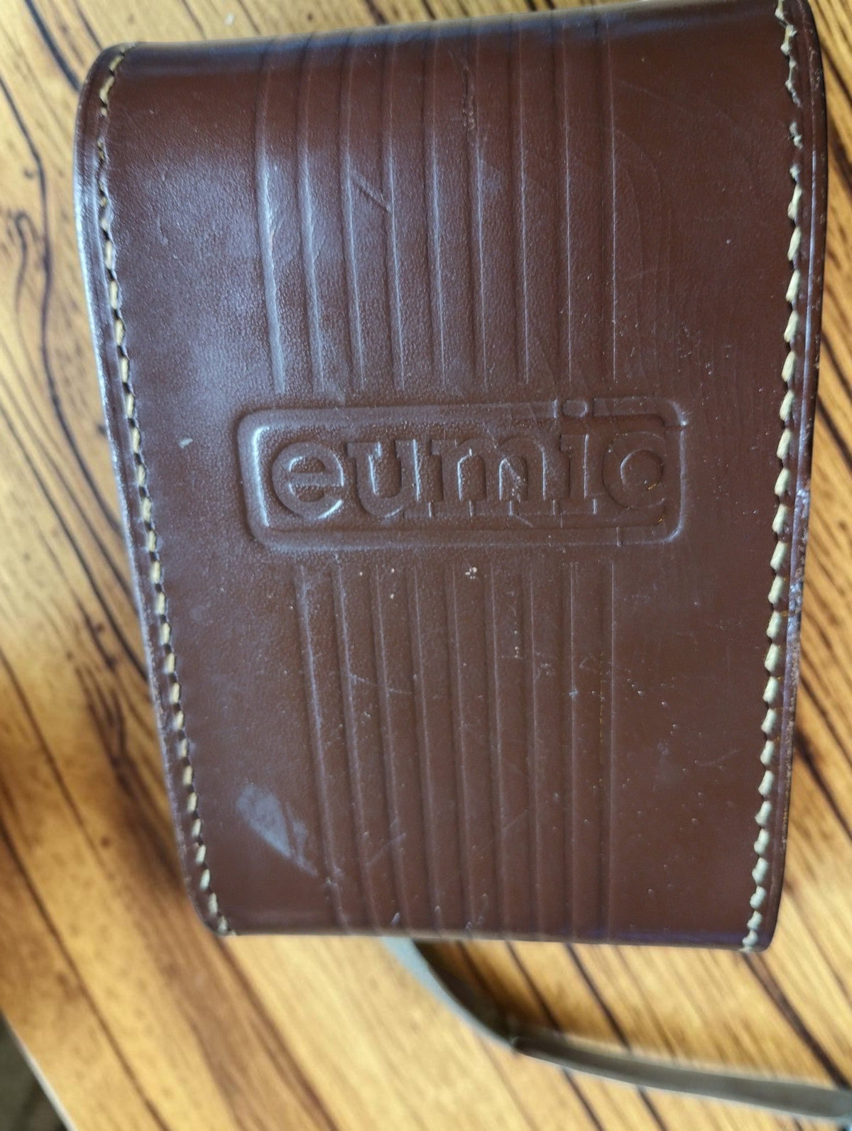 Close-up of the embossed Eumig logo and stitched edges on the brown leather camera case
