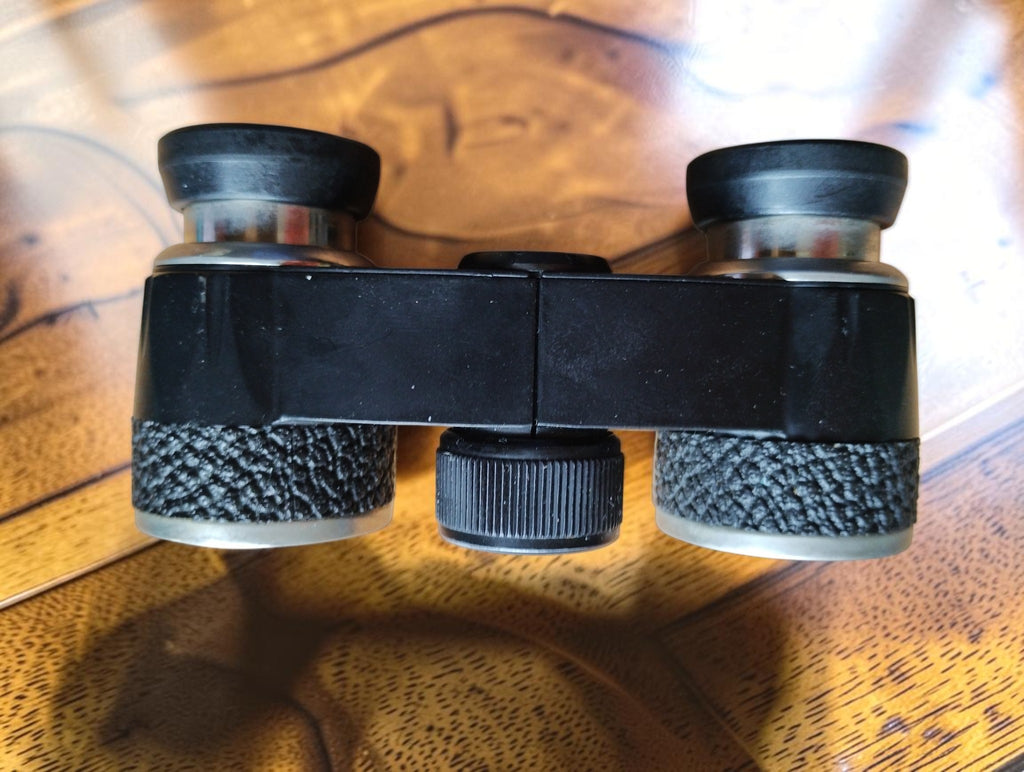 Side view of vintage Aida opera glasses showing the central focusing wheel and textured black grips
