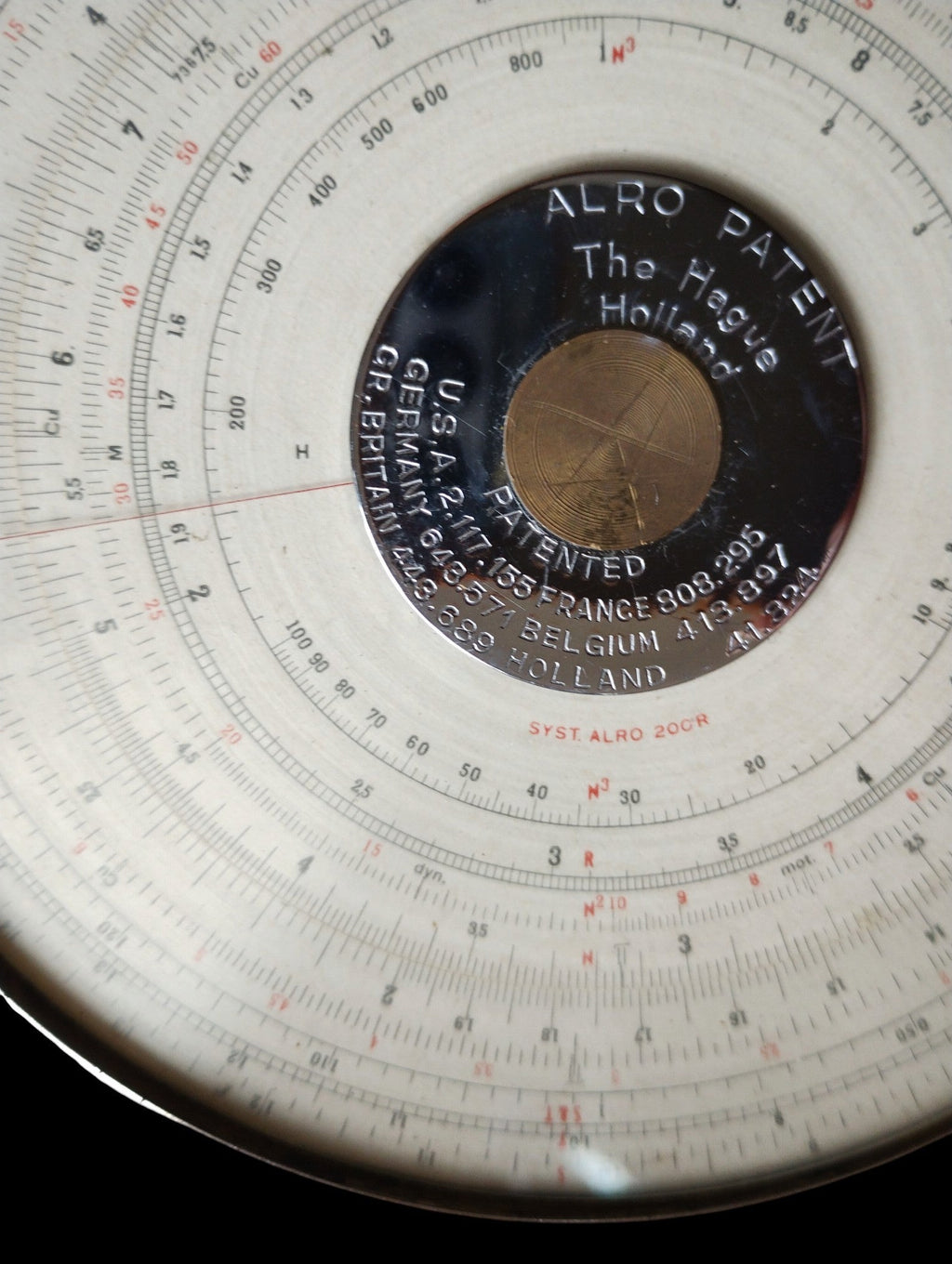 Close-up of the ALRO 200R circular slide rule showing the ALRO Patent plate, The Hague Holland marking and graduated scales.
