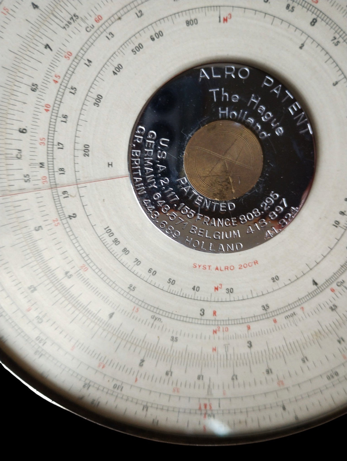 Close-up of the ALRO 200R circular slide rule showing the ALRO Patent plate, The Hague Holland marking and graduated scales.

