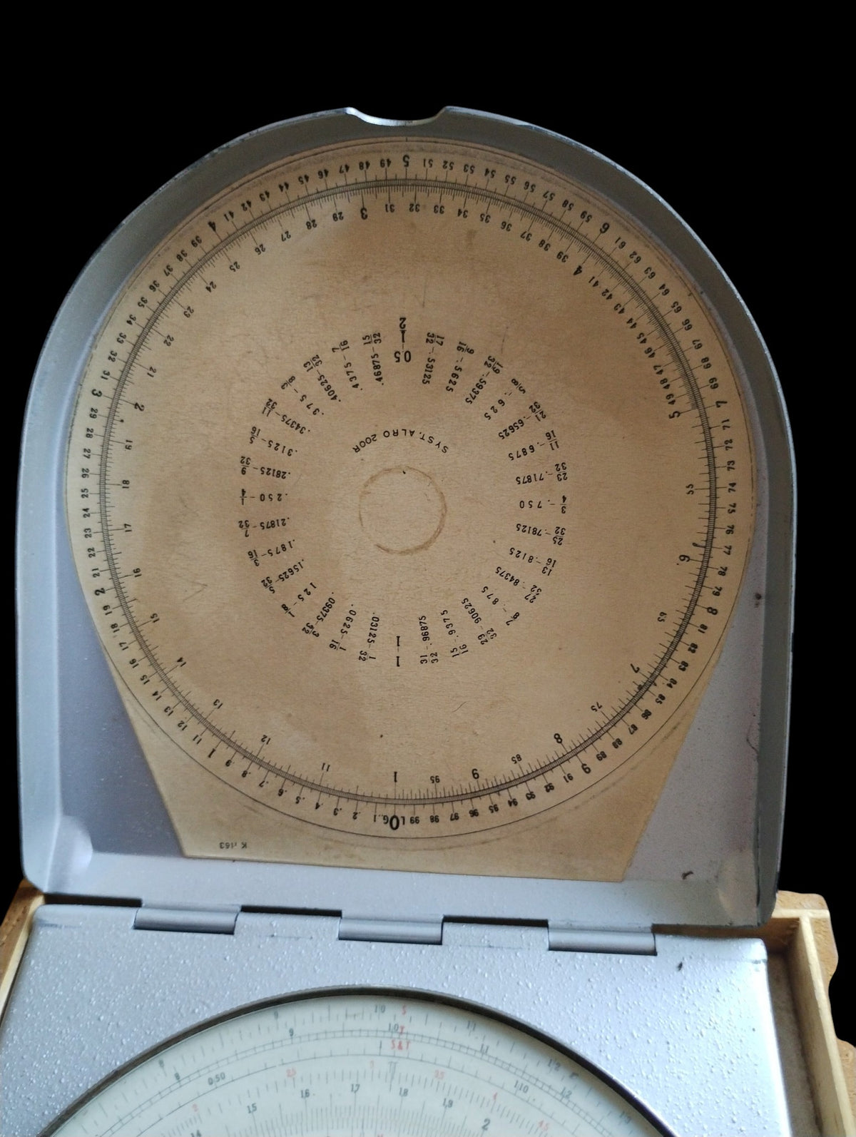 Circular reference scale inside the hinged metal lid of the ALRO 200R slide rule, showing age-related discoloration.

