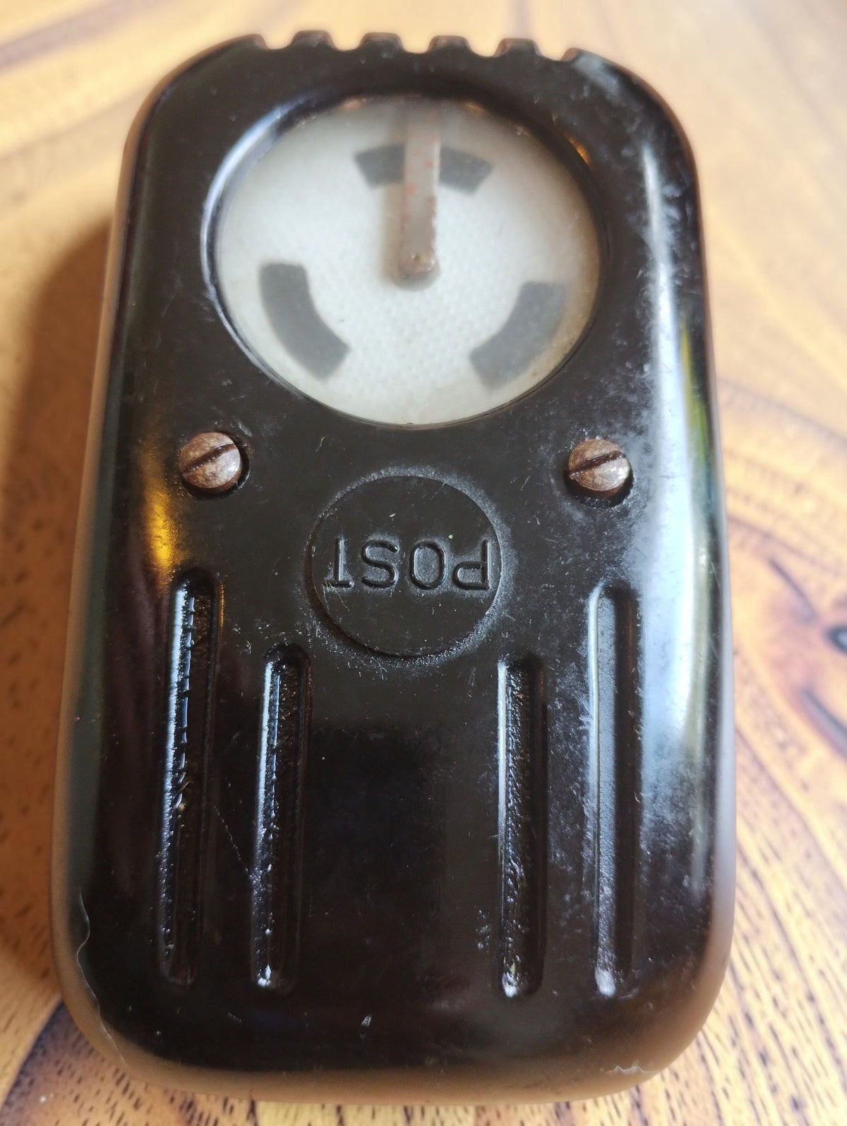 Vintage POST line tester with a round indicator window and ribbed black Bakelite housing, front view.
