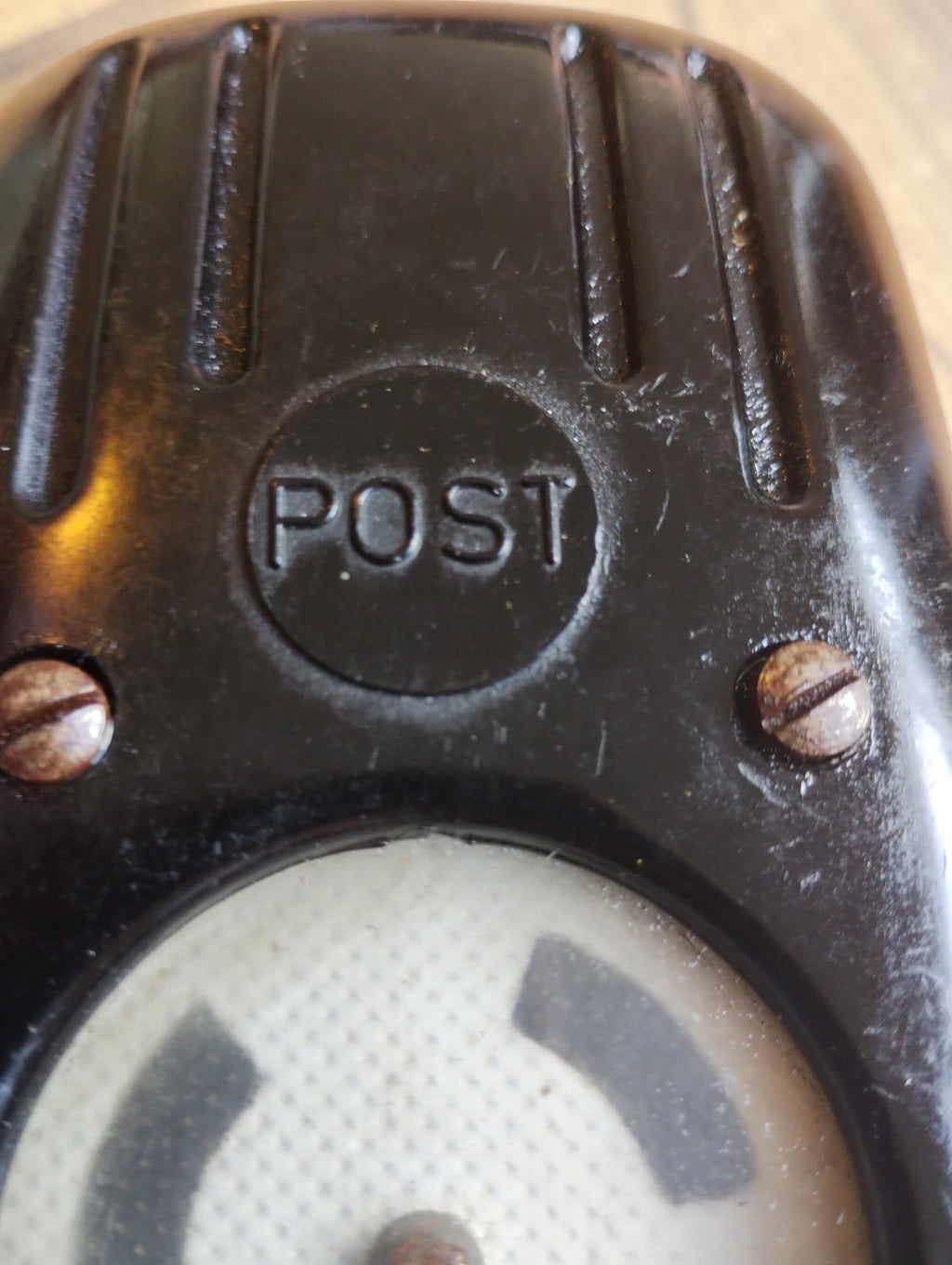Close-up of the molded POST logo, slotted screws and surface wear on the black Bakelite line tester.
