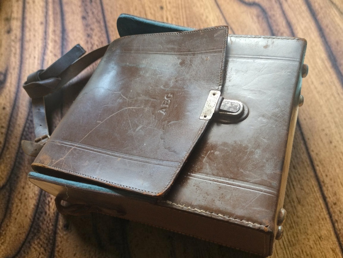 Brown leather carrying case with an embossed AEG logo, metal clasp and visible age-related wear
