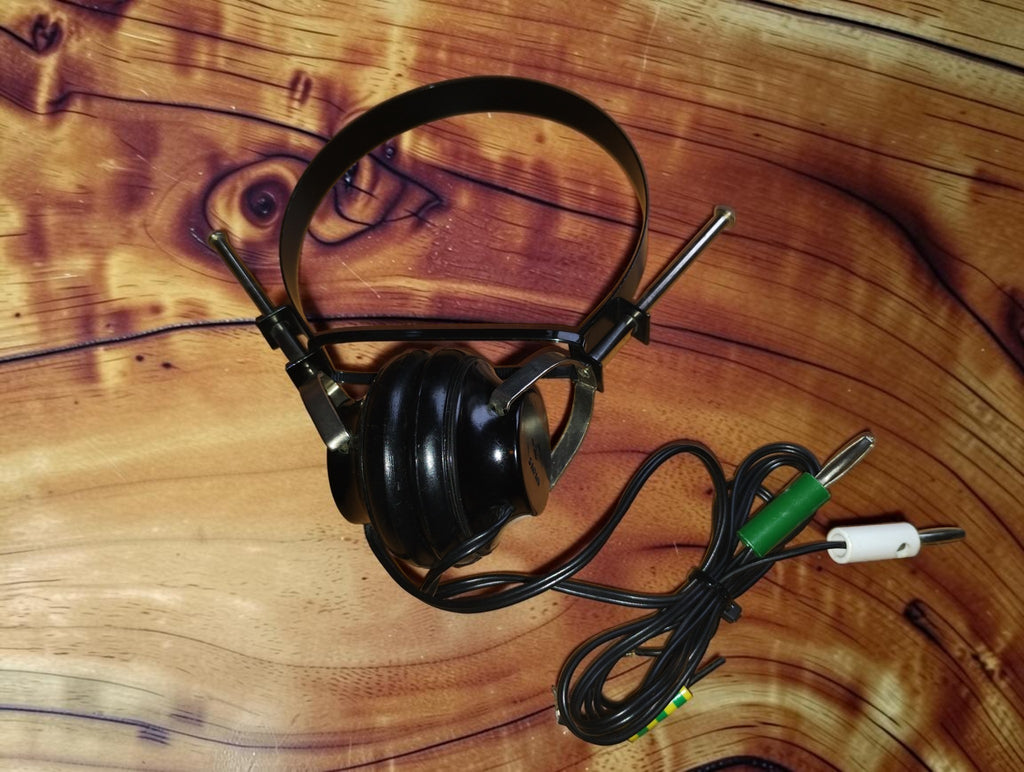 Vintage S.F. mono headphone made in Japan, with black steel headband, single black earcup, and a cord ending in green and white banana plugs.
