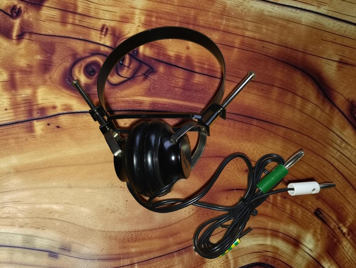 Vintage S.F. mono headphone made in Japan, with black steel headband, single black earcup, and a cord ending in green and white banana plugs.
