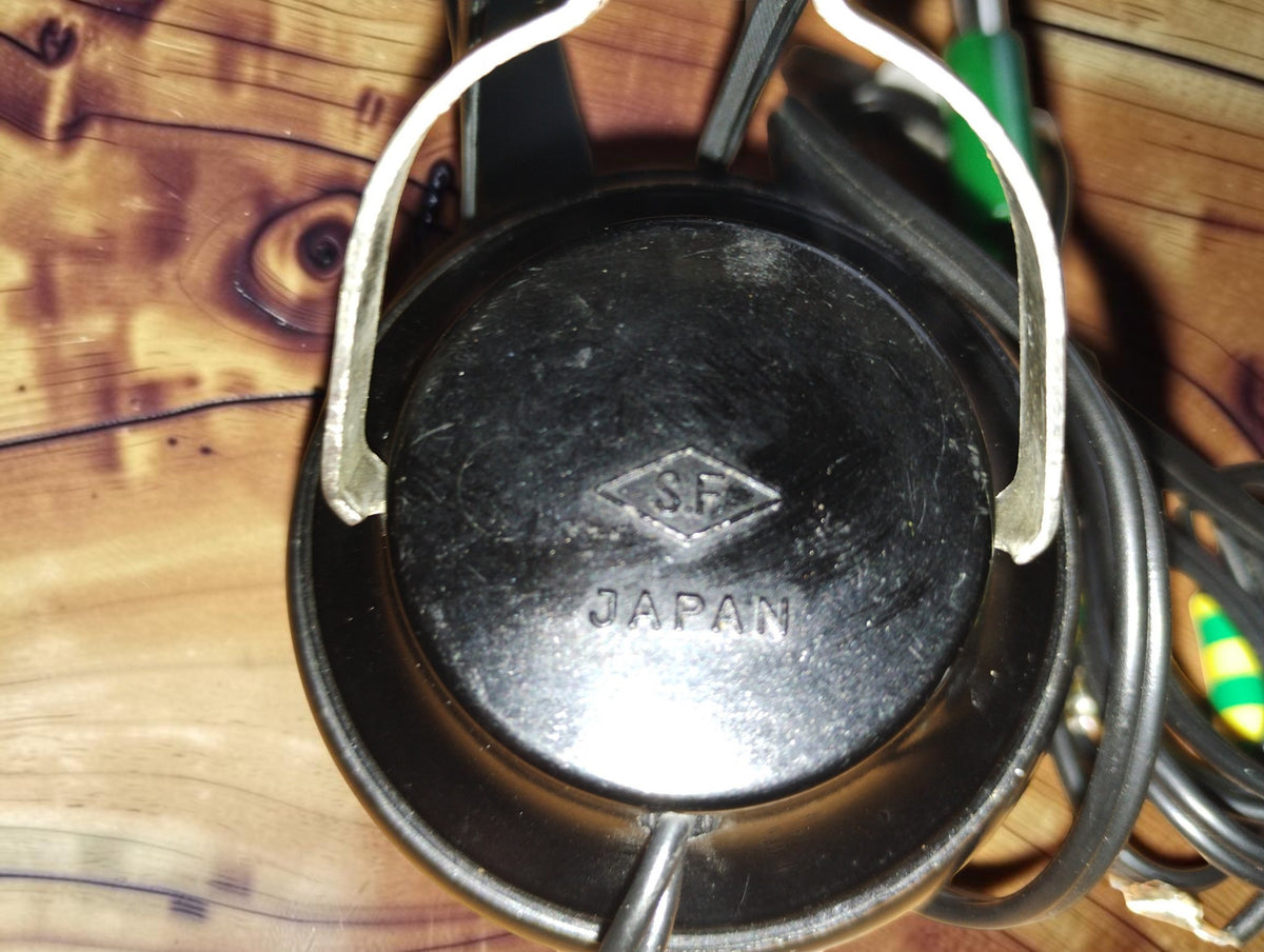Close-up of the black earcup of a vintage S.F. headphone, showing the embossed S.F. diamond logo and JAPAN marking.
