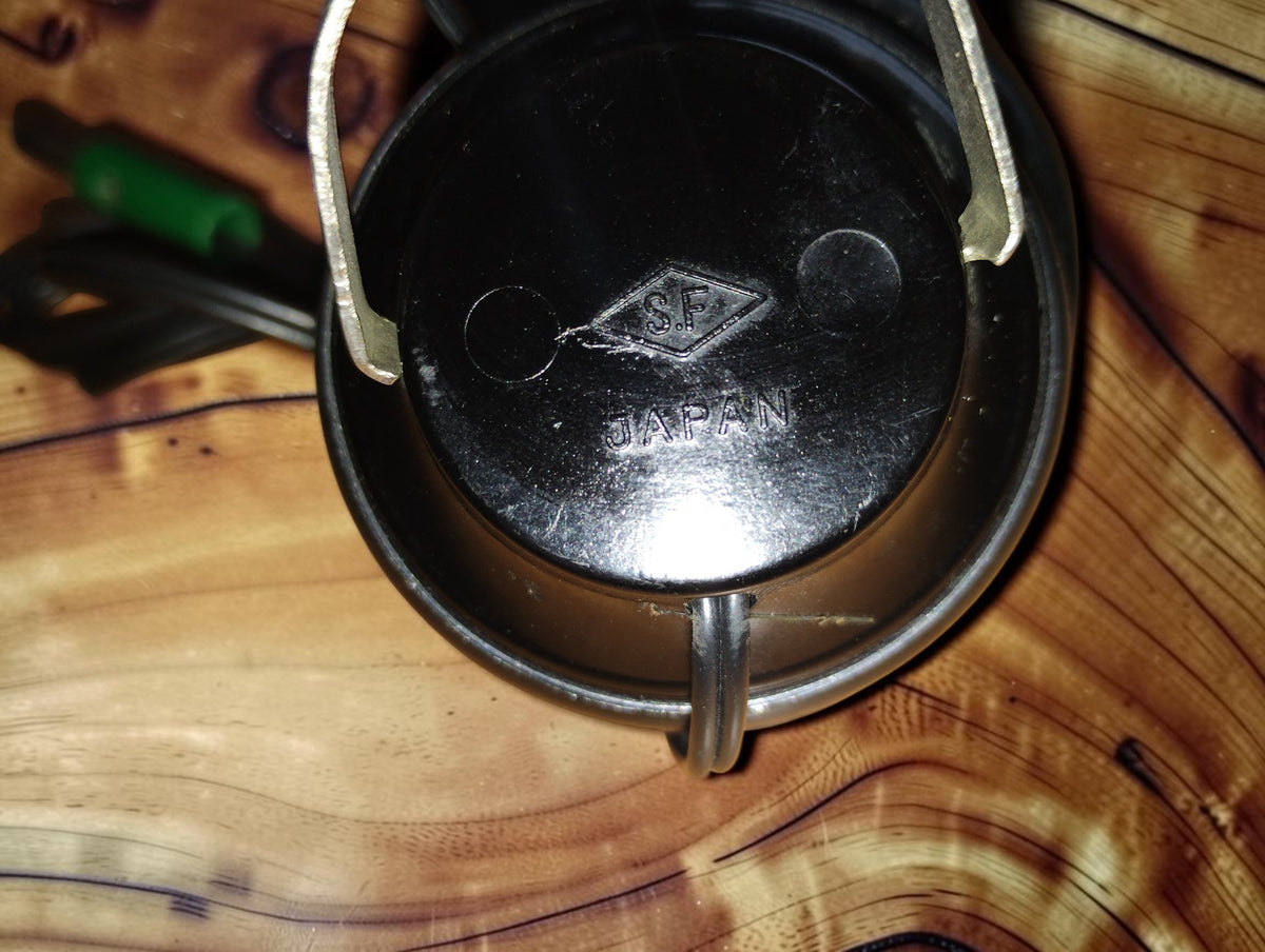 Close-up of the black earcup of a vintage S.F. headphone, with the S.F. diamond logo and JAPAN marking and the metal headband above.
