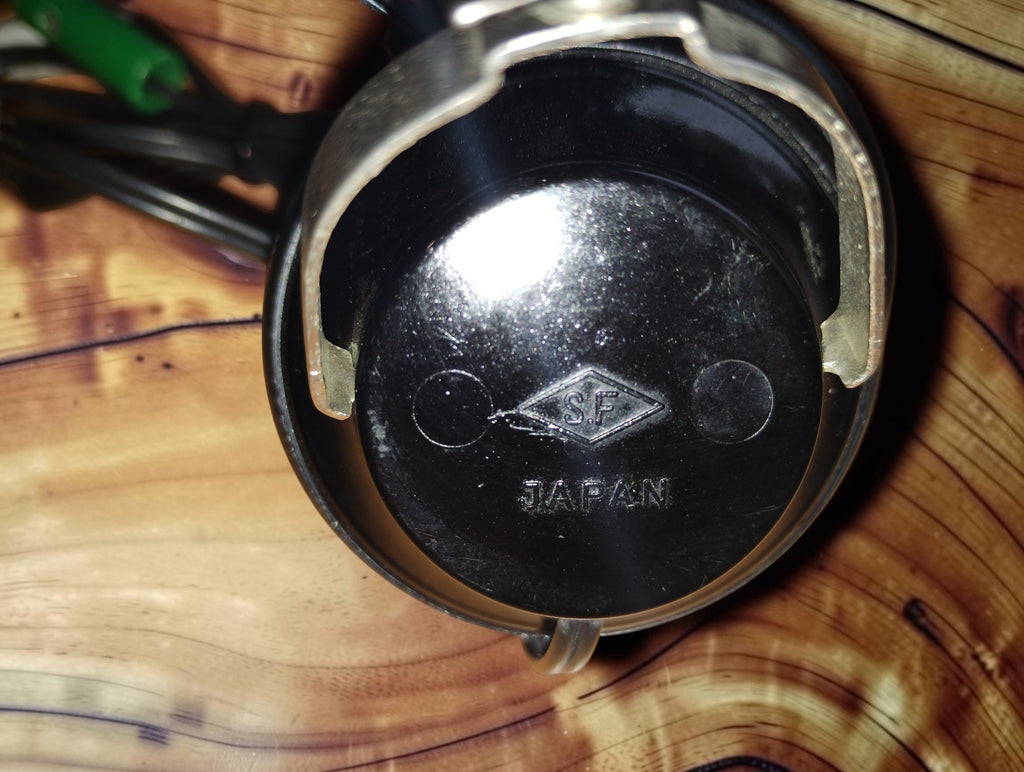 Close-up of the glossy black earcup of a vintage S.F. headphone, with the embossed S.F. diamond logo and JAPAN marking visible.
