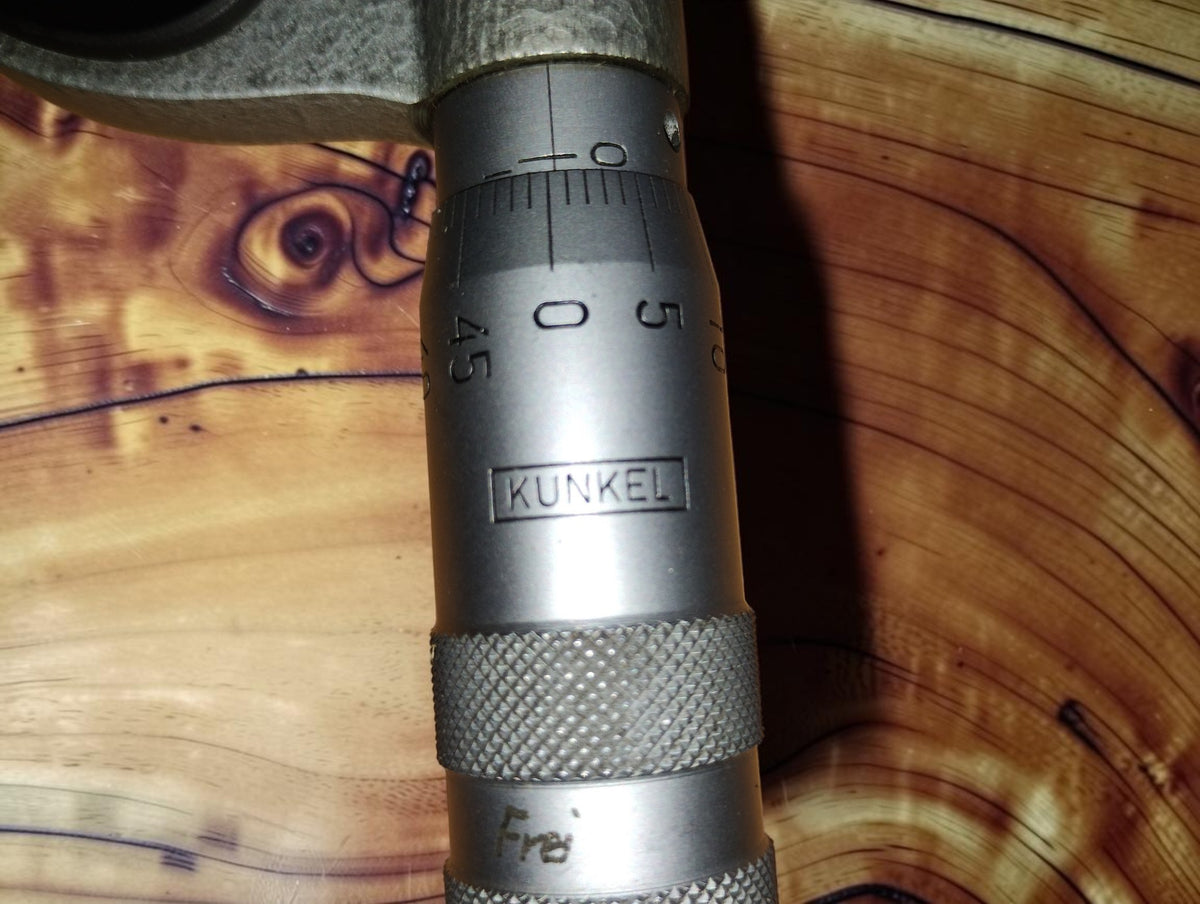 Close-up of the KUNKEL maker's mark, graduated scale and knurled adjustment rings on the vintage disc micrometer.
