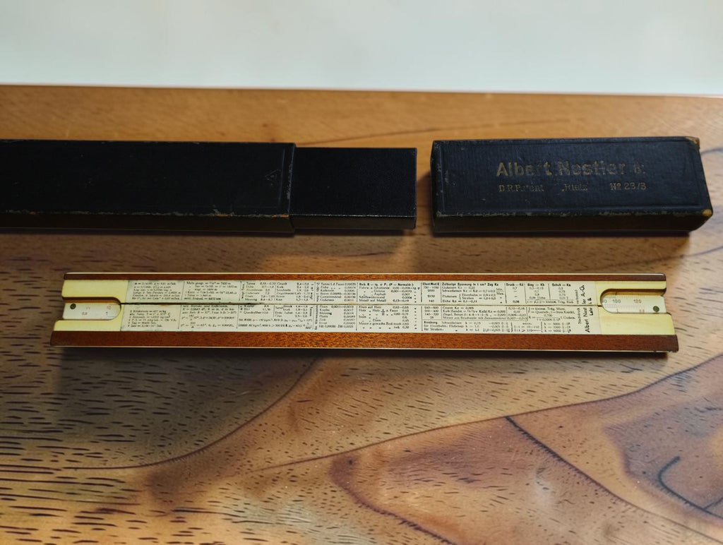 Back of Albert Nestler slide rule showing reference tables, with the black sliding case open above it
