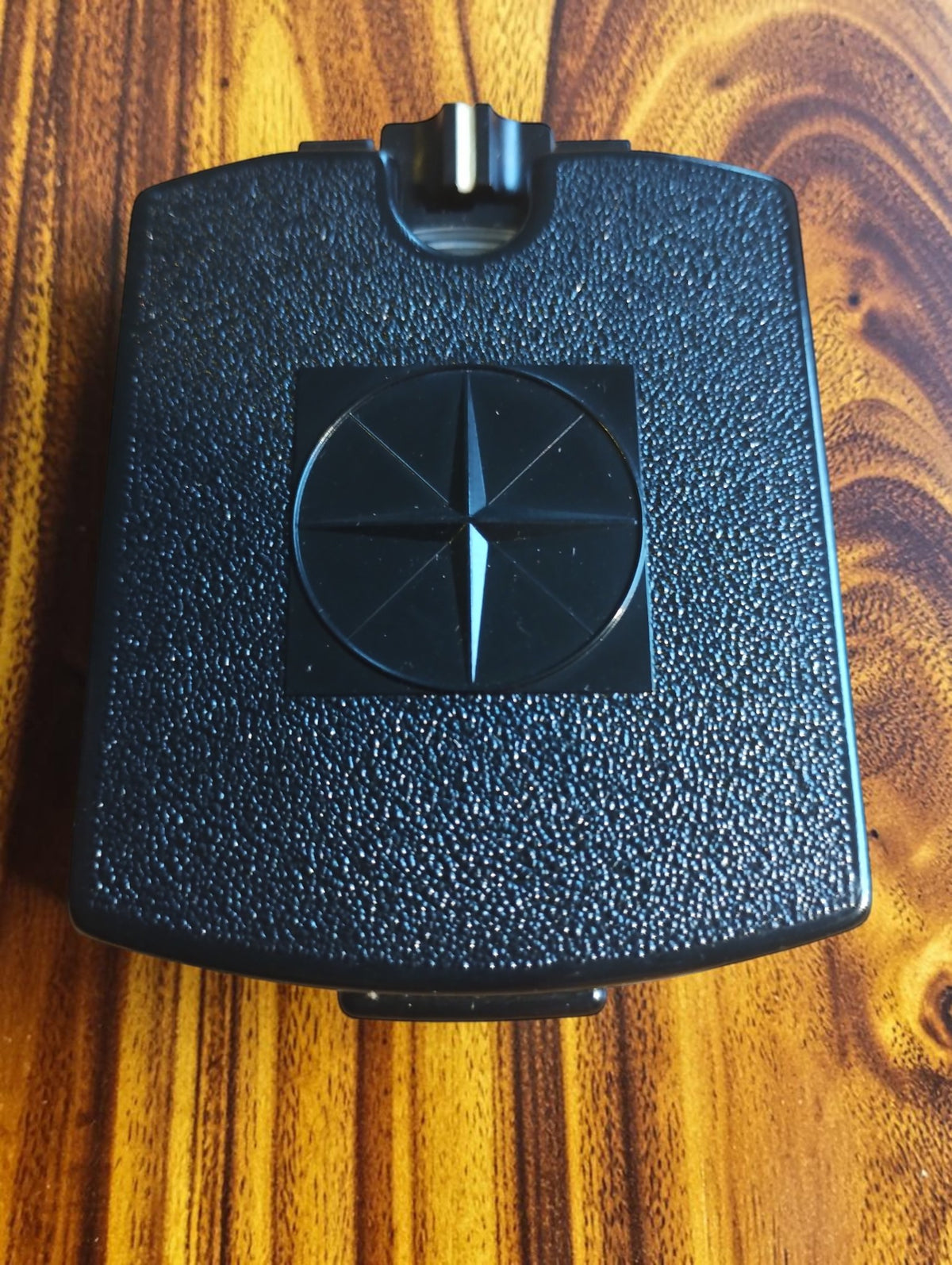 Closed vintage mirror compass with a textured black case and raised compass rose on the lid

