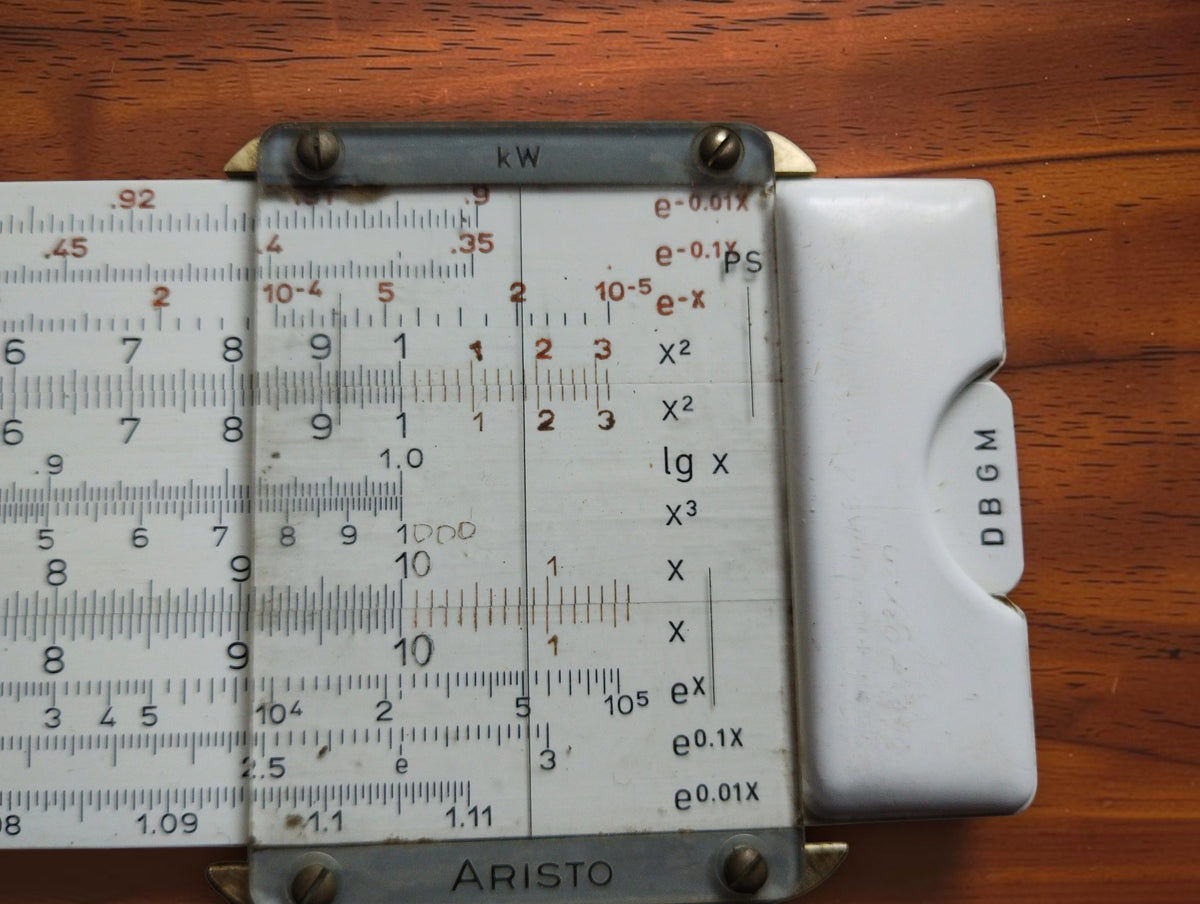 Close-up of the ARISTO Studio slide rule cursor, logarithmic scales, and DBGM marking.
