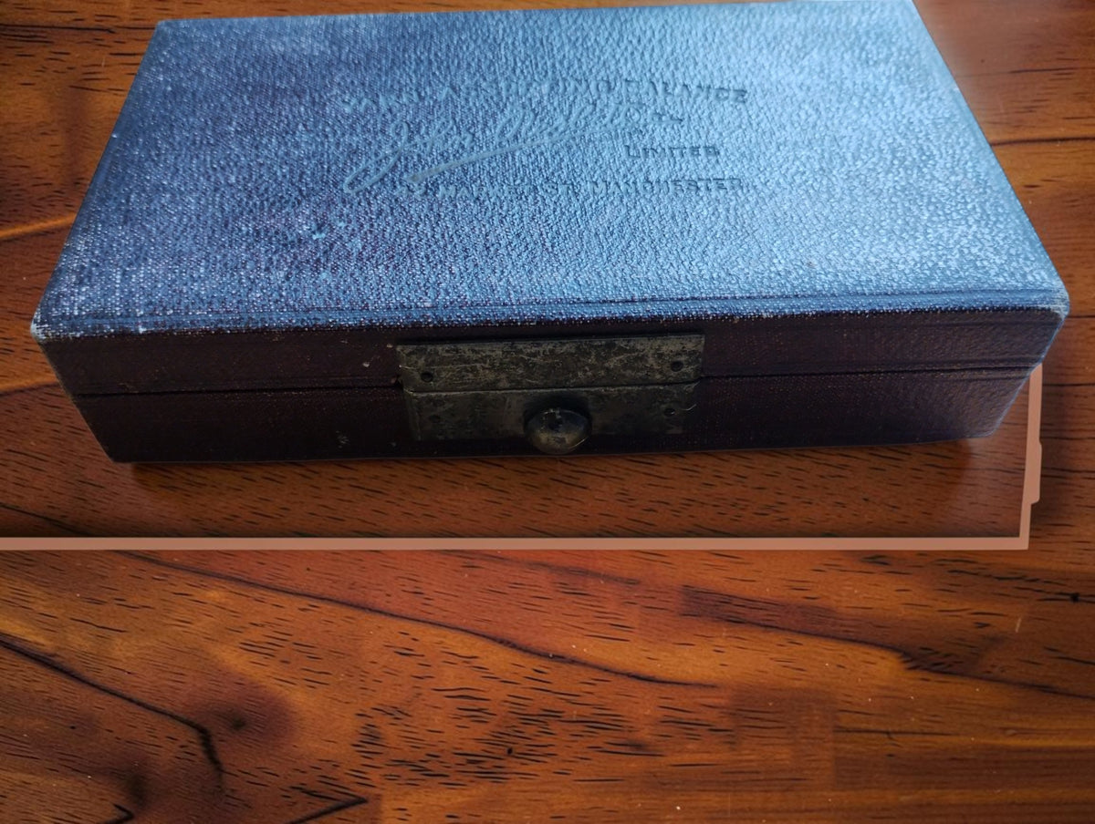 Closed textured presentation case with front clasp for the John Nesbitt textile yarn balance.
