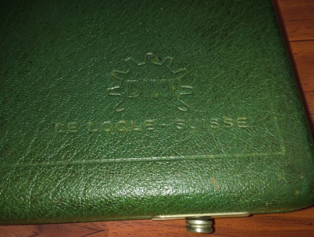 Close-up of the embossed DIXI gear logo and Le Locle Suisse lettering on the green watchmaking tool case
