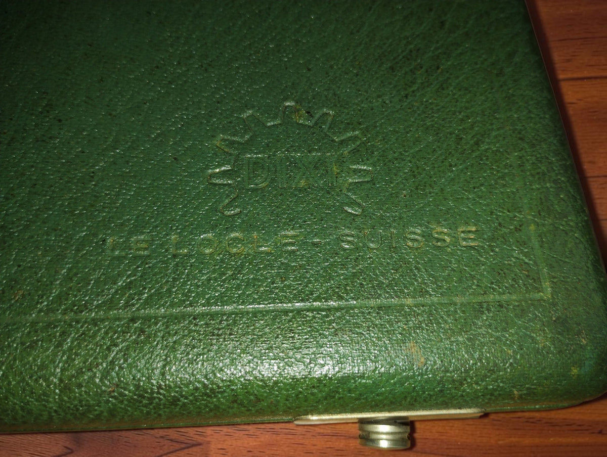 Close-up of the embossed DIXI gear logo and Le Locle Suisse lettering on the green watchmaking tool case
