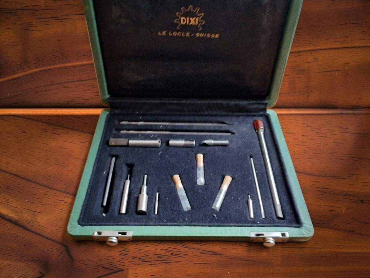 Open DIXI Le Locle watchmaking tool set with precision tools and three cork-stoppered glass tubes in a fitted black tray

