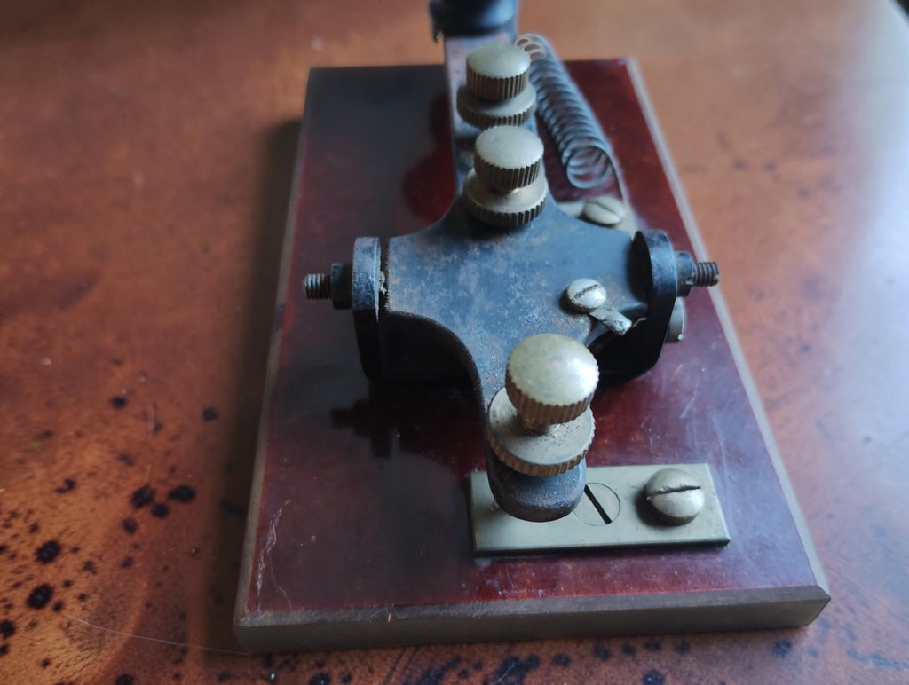 End view of the antique Morse telegraph key, showing the knurled adjustment screws, pivot assembly and mounting plates.
