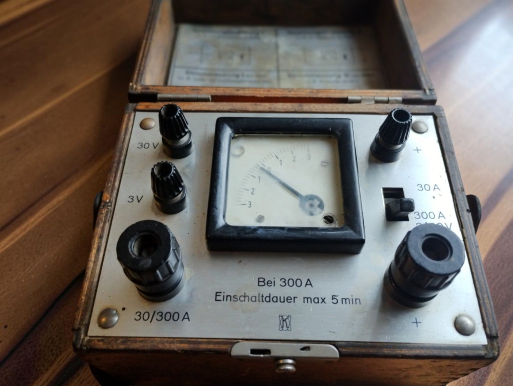 Vintage DC volt and amp meter in an open wooden case, showing the analog dial, black terminals and 3/30 V and 30/300 A markings.
