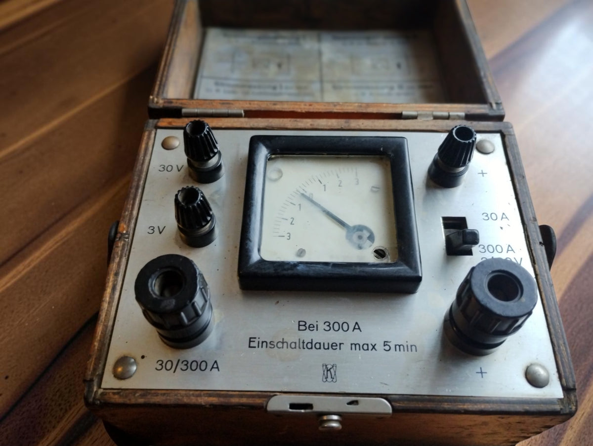 Vintage DC volt and amp meter in an open wooden case, showing the analog dial, black terminals and 3/30 V and 30/300 A markings.
