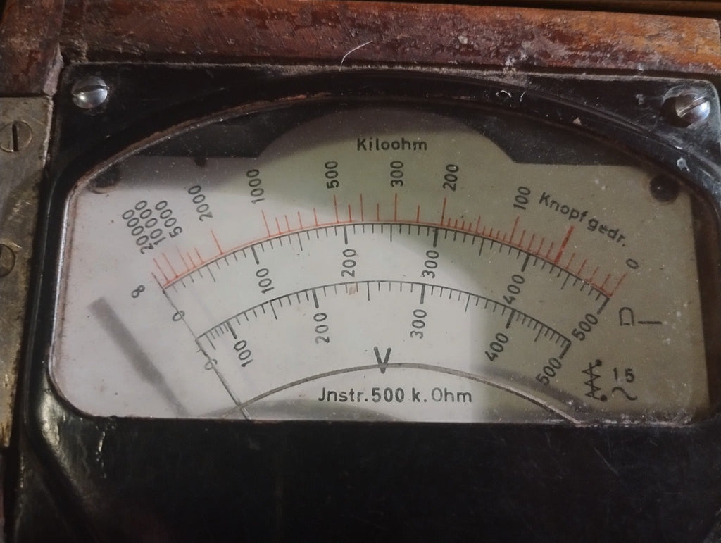 Close-up of the insulation tester dial with voltage and kilohm scales and German operating markings.
