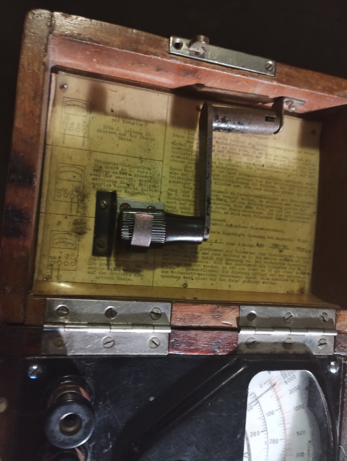 Open wooden lid containing a folding metal crank and an original German instruction sheet for the insulation tester.
