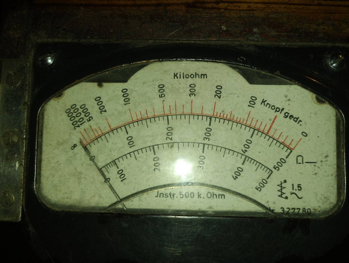Detailed view of the curved analog scales, kilohm markings, and aged dial face of the German insulation tester.

