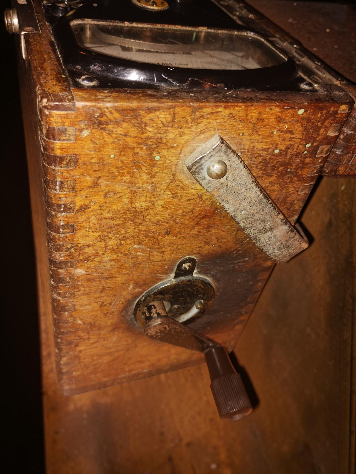 Side of the wooden insulation tester case, showing dovetail joints, the crank fitting, and a worn leather carrying strap.
