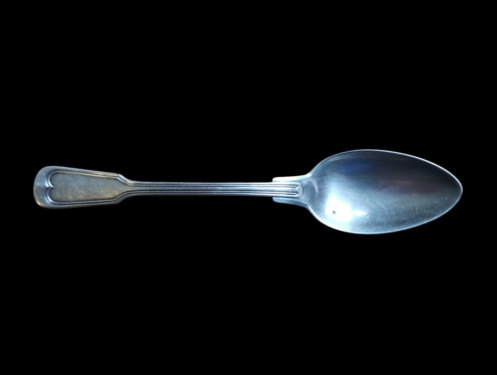 Front view of a vintage spoon with an outlined handle pattern and visible surface discoloration
